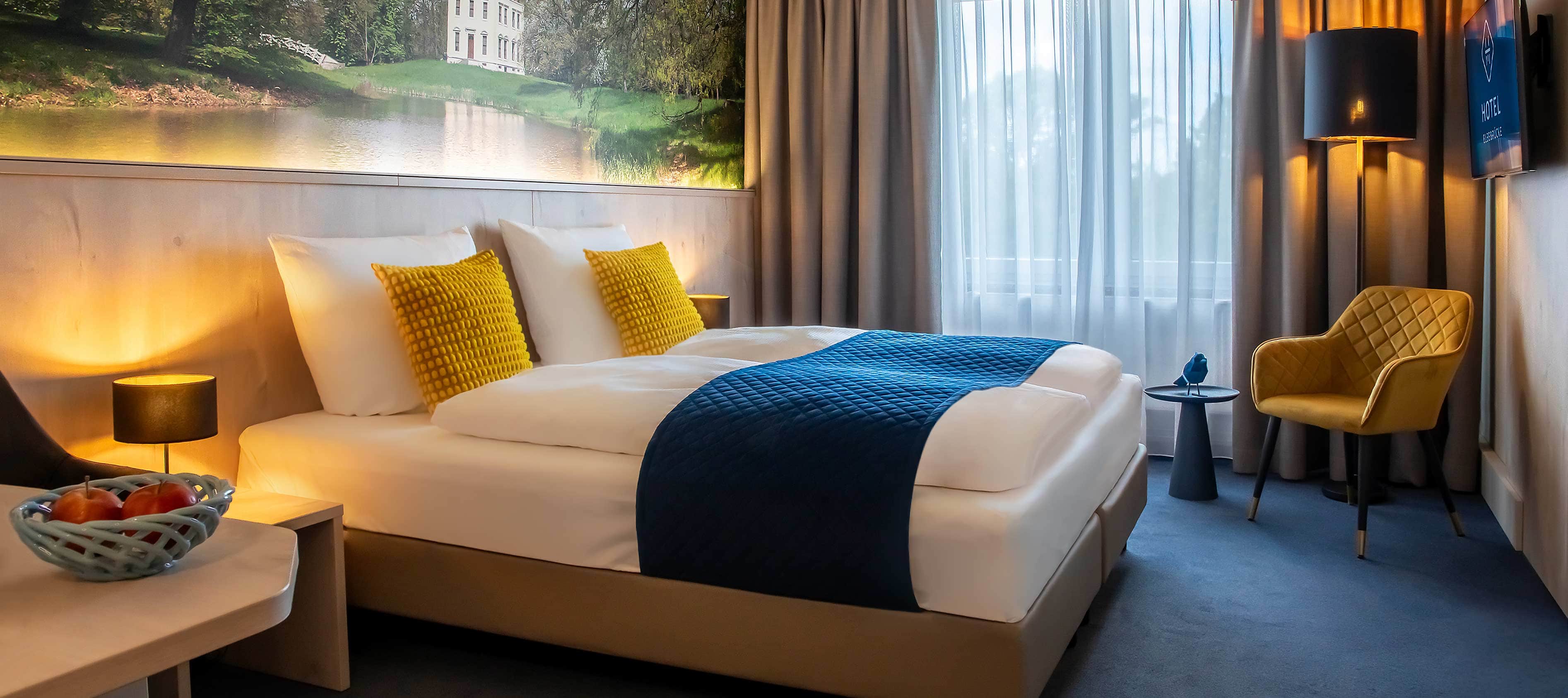 Foto eines einladenden Hotelzimmers im Hotel Elbebrücke bei Dessau, ausgestattet mit Doppelbett, TV und Loungesessel