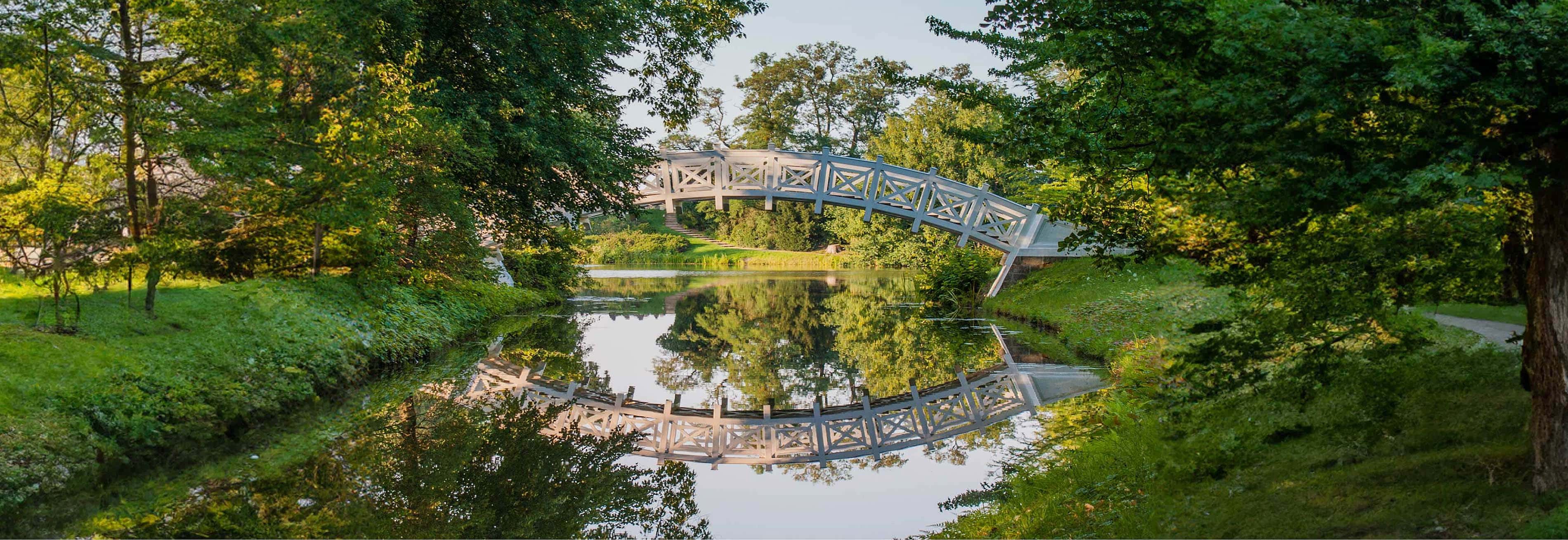 Idyllische Aufnahme einer weißen Brücke die einen Fluss überspannt und in ihm gespiegelt wird, unweit des Hotels Elbebrücke bei Dessau