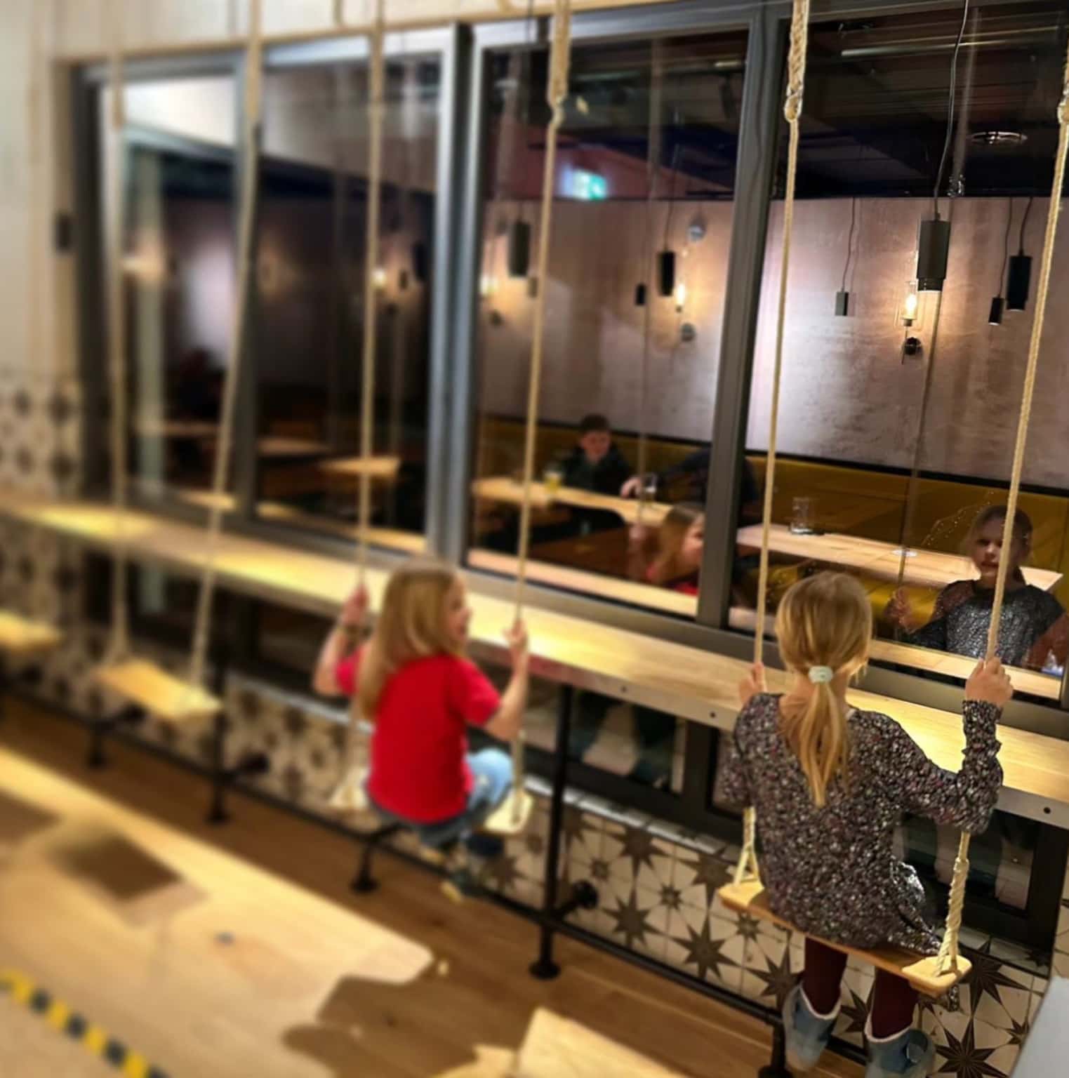 Foto von vier Schaukeln in einem Restaurant bei Dessau, auf zwei von ihnen schaukeln zwei junge Mädchen vor einer Fensterfront