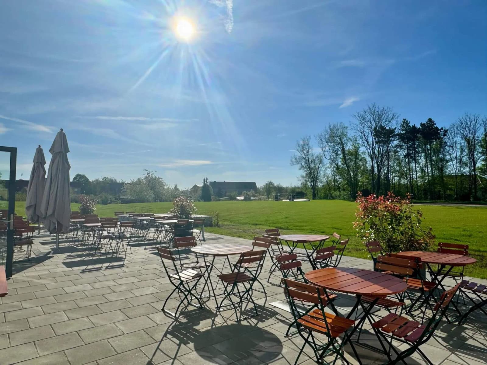 Foto vom Außenbereich des Restaurant Elbebrücke bei Dessau, auf dem mehrere hölzerne Tische und Stühle stehen und der von Rasen umgeben ist
