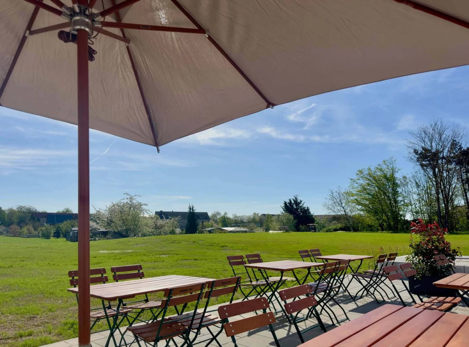Aufnahme vom großzügigen Außenbereich einer Eventlocation in Sachsen-Anhalt mit einer großen Grünfläche, Tischen und Stühlen