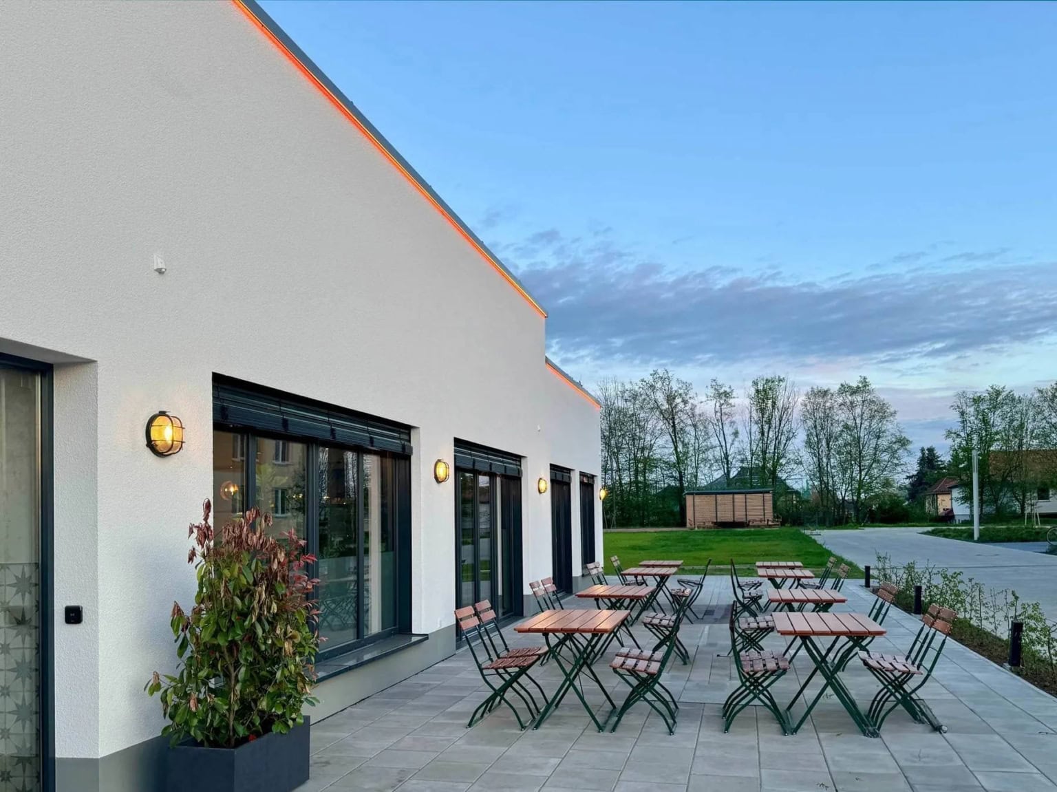 Blick auf eine sehr große Außenterrasse eines Restaurants bei Dessau mit mehreren Holztischen und Stühlen, aufgenommen bei Dämmerung