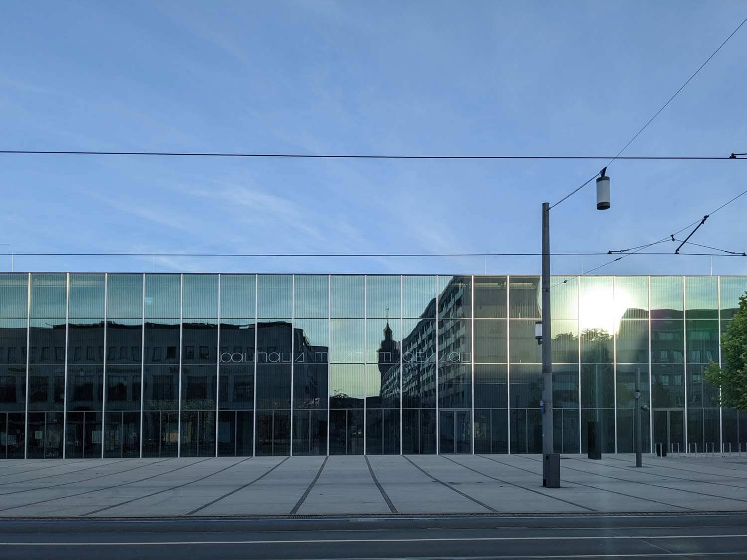 Foto der gläsernen Außenfassade des Bauhaus-Museums, eine der Sehenswürdigkeiten in Dessau, in der sich die Sonne spiegelt