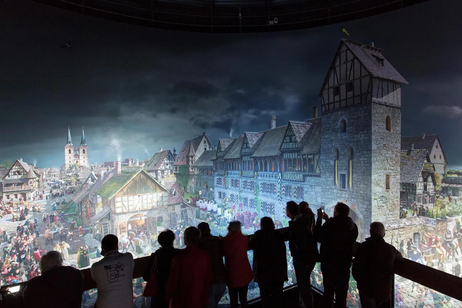 Mehrere Personen stehen auf einer Plattform und bewundern eine Lichtprojektion, die die Lutherstadt Wittenberg im Jahre 1517 zeigt