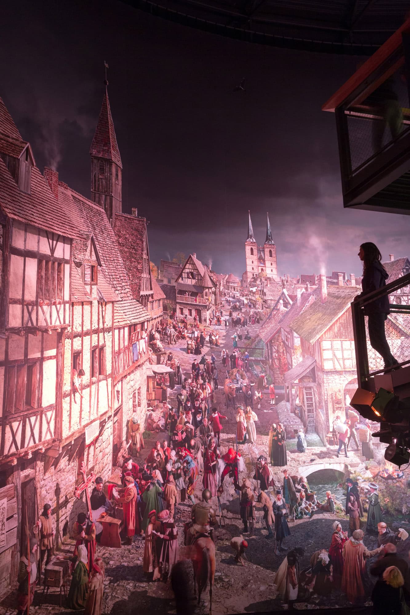 Eine Frau steht im Rahmen ihres Urlaubs in Wittenberg an einem Geländer und schaut auf eine Lichtinstallation einer mittelalterlichen Stadt