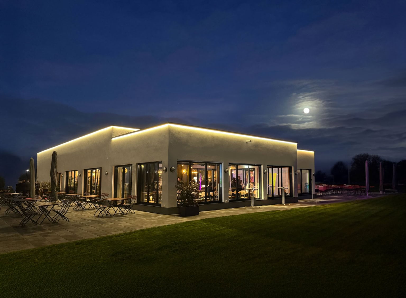 Beleuchtetes Restaurant Elbebrücke bei Dessau, ringsherum ist der große grüne Außenbereich und der Mond zu sehen