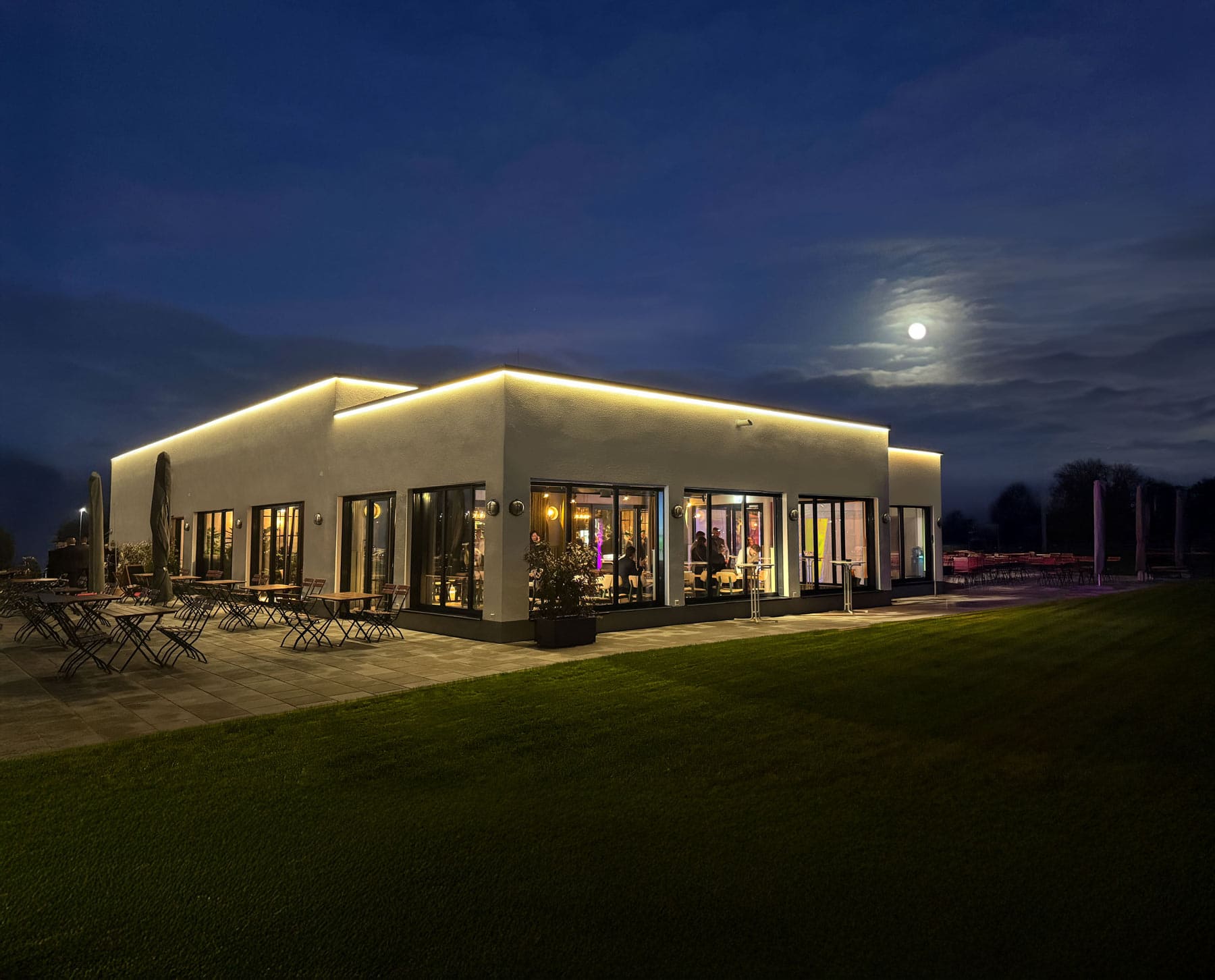 Beleuchtetes Restaurant Elbebrücke bei Dessau, ringsherum ist der große grüne Außenbereich und der Mond zu sehen