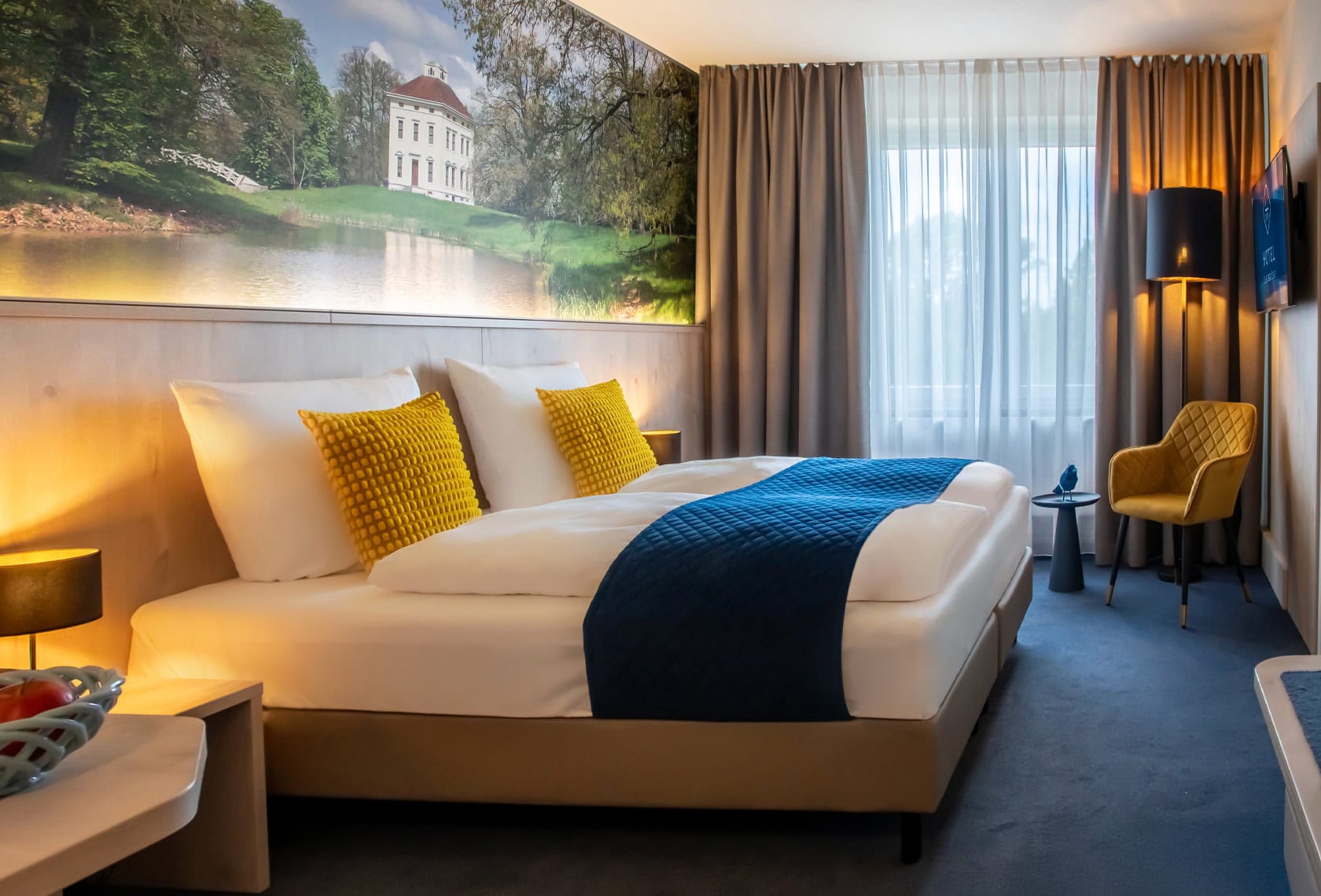 Aufnahme eines barrierefreien Hotelzimmers mit bequemen Doppelbett, TV und angrenzendem Badezimmer im Hotel Elbebrücke