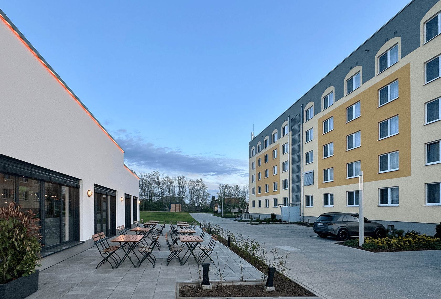 Blick auf eine sehr große Außenterrasse eines Restaurants bei Dessau mit mehreren Holztischen und Stühlen, aufgenommen bei Dämmerung
